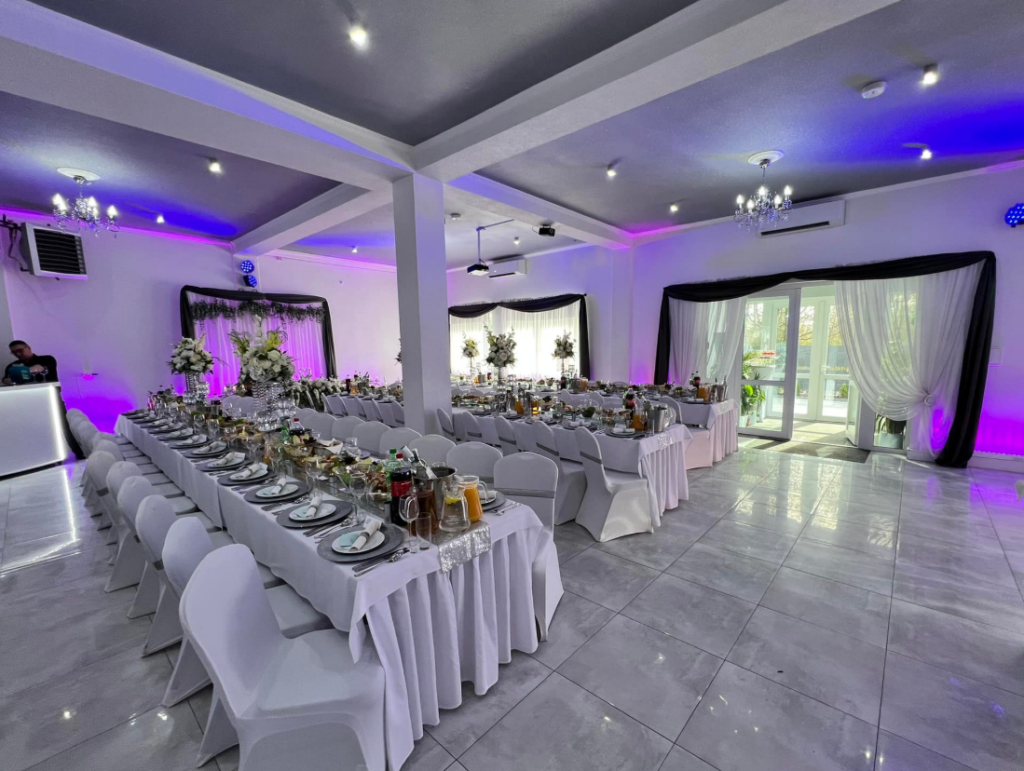 Elegancka sala bankietowa z dekoracją stołów, oświetleniem LED i przygotowaniem do przyjęcia okolicznościowego.